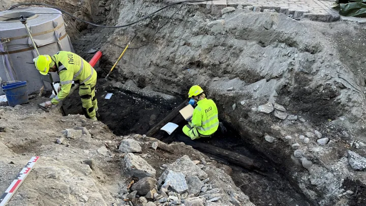 To personer undersøker et gammel tredekke som er gravd fram.