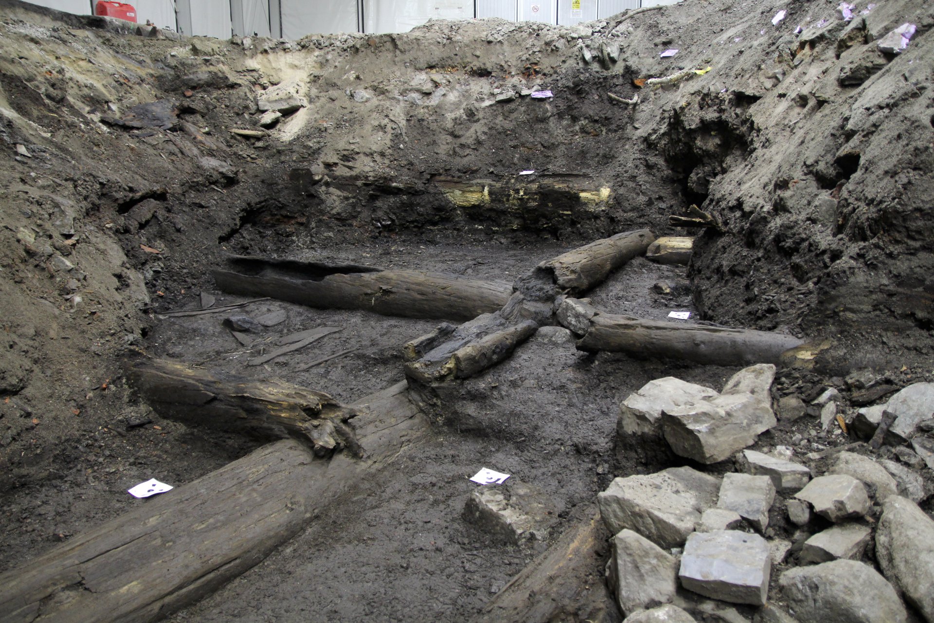 Utgravd grop med gamle trestokker og stein.